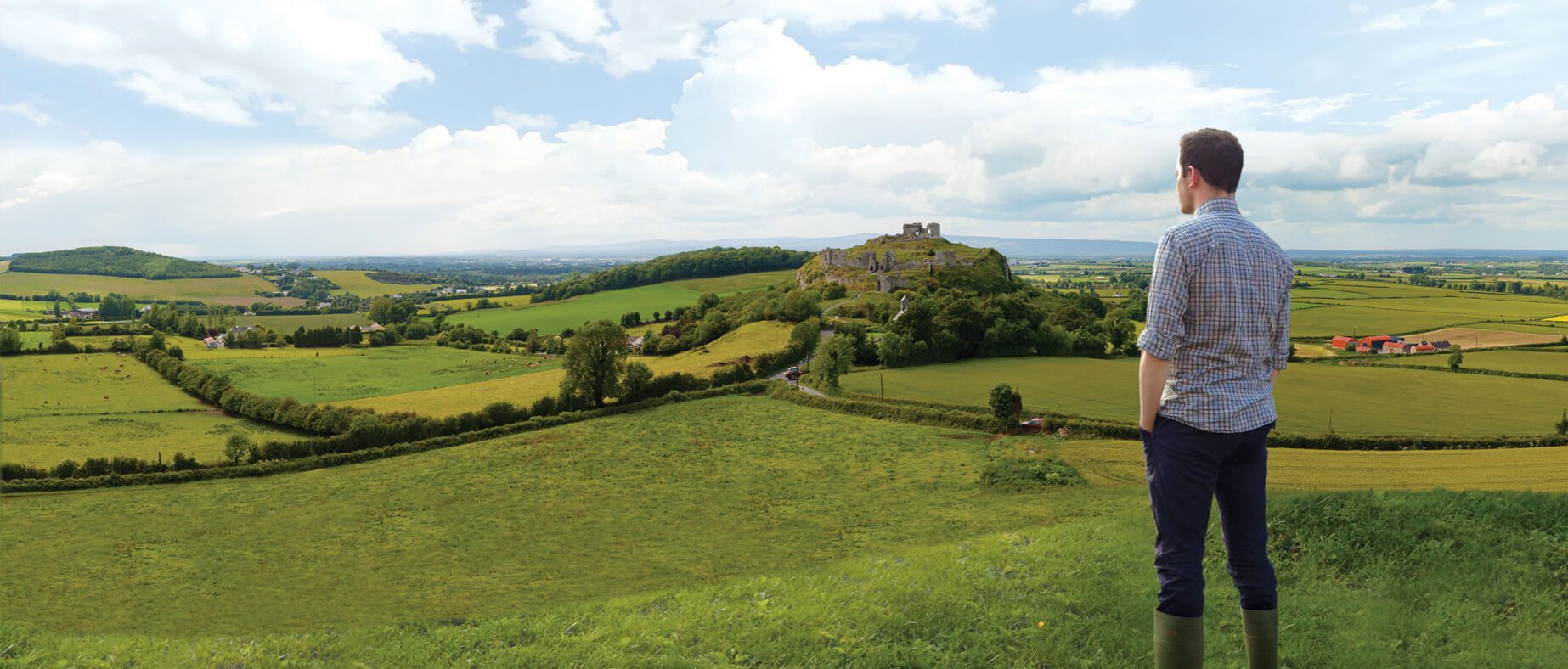 there is a man looking over green fields in the centre there is some type of old ruin
